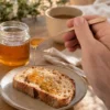 Handgefertigter Honiglöffel aus Nussbaum lässt Honig auf eine Scheibe Brot fließen