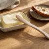 Handgefertigtes Streichmesser aus Birke mit Butter und Brot auf einem Holztisch